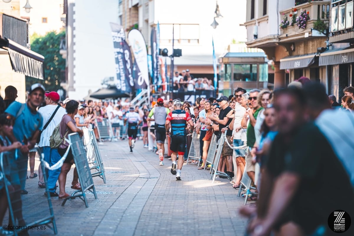 Iván corriendo de espaldas por el centro de Zarautz con el ambiente de la carrera a pie